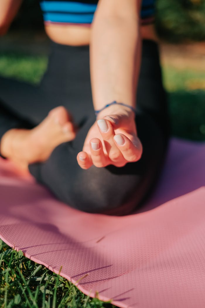 team-02 Close-up of a woman meditating in the lotus position on a pink yoga mat outdoors.